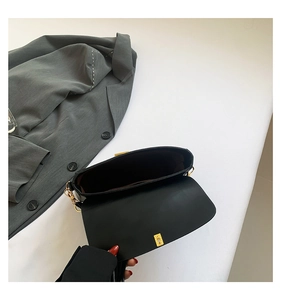 Top view of black leather crossbody bag interior with gold buckle and grey blazer background