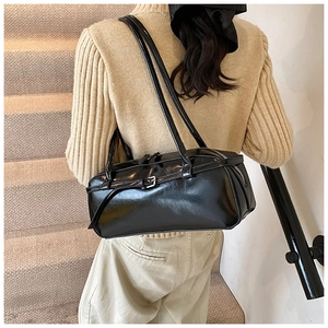 Detail view of a black glossy shoulder bag with metal buckle on a neutral background