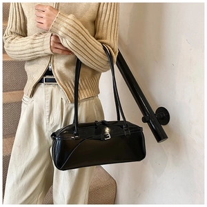 Close-up of black patent leather shoulder bag with decorative buckle and sleek finish