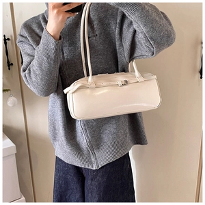 Detail of a creamy white cylindrical baguette bag with silver buckle and adjustable strap