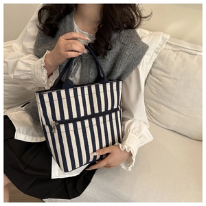 Detail of navy striped canvas tote bag with front zipper pocket held by model