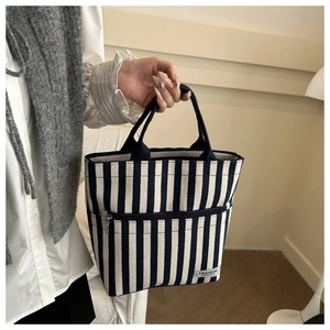 Detail of striped canvas tote bag featuring front zipper pocket and fashion logo label