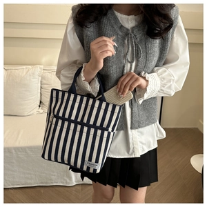 Detail of striped canvas tote bag showing zipper pockets and fashion instinct brand label