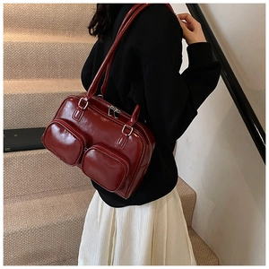 Close-up of deep red glossy shoulder bag with dual front pockets and zipper detail
