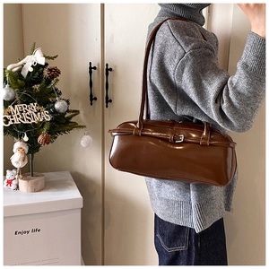 Detail of a deep brown shiny PU leather baguette shoulder bag with silver buckle accent