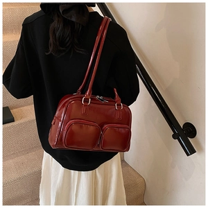 Detail of dark red patent leather shoulder bag with two front zipper pockets and long straps