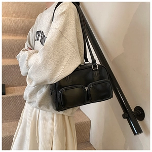 Detail of black faux leather underarm bag featuring dual front zipper pockets on a model