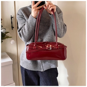 Detail of burgundy patent leather baguette bag with buckle and dual zipper design
