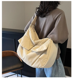 Detail view of a large cream-colored canvas crossbody bag with two functional front pockets