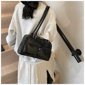 Detail view of glossy black faux leather shoulder bag featuring dual front zipper pockets