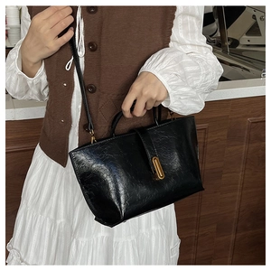 Détail d'un sac à main noir brillant vintage avec boucle dorée sur fond de bois