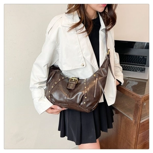 Détail du sac croissant rétro marron foncé avec rivets dorés et texture en cuir brillant