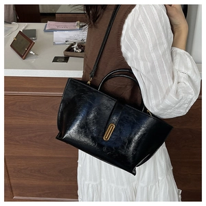 Detail of black glossy leather tote bag with gold metal lock and elegant folded texture