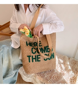 Detail of woven tote bag with green 'HERE COMES THE SUN' embroidery and strap