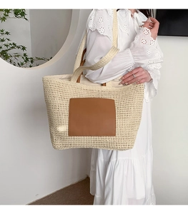 Detail of a large straw tote bag with brown leather patch and white woven texture