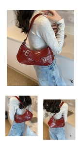 Detail view of red motorcycle-style crescent shoulder bag with silver metallic eyelet buckles