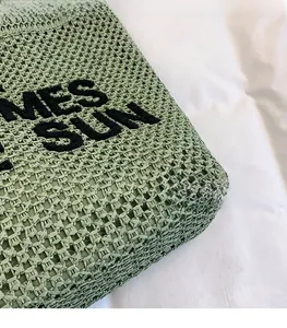 Close-up of green woven straw beach bag with black embroidered lettering detail