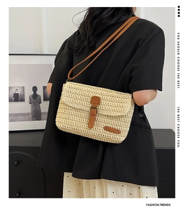 Detail of a beige woven straw crossbody bag with brown faux leather strap on model