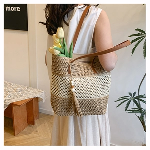Detail of hand-woven straw tote bag with brown leather straps and chic tassel decor