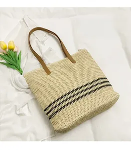 Detail of woven straw tote bag with black stripes and brown leather strap on white cloth