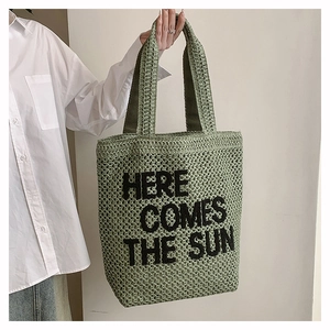 Detail of green woven tote bag featuring black Here Comes The Sun text embroidery