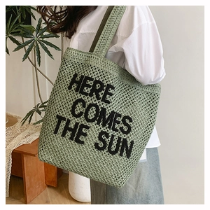 Green woven tote bag with 'HERE COMES THE SUN' slogan shown on model in natural lighting