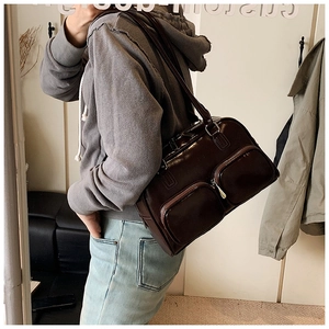 Detail view of dark brown faux leather underarm bag with double front pockets and metal zippers