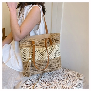 Detailed texture of the woven straw tote bag with brown leather handles and tassel accent