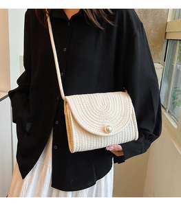 Detail view of woven straw shoulder bag featuring a large pearl clasp and textured flap