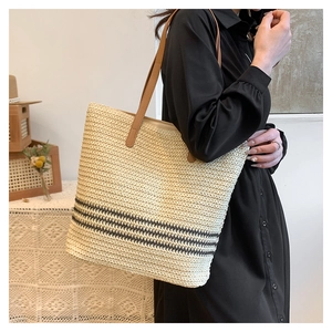 Straw tote bag with brown leather straps and black stripes in a lifestyle setting