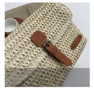 Close-up of woven straw bag detail featuring brown leather strap and bronze buckle closure