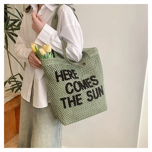 Detail of green woven tote bag with 'HERE COMES THE SUN' embroidery and texture