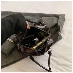 Top view of deep brown patent leather underarm bag with zipper on a grey wool coat