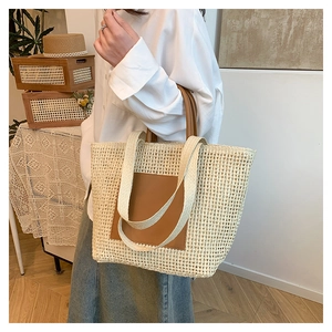 Detail of a large straw tote bag with brown leather patch and dual woven shoulder straps