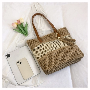 Close-up of woven straw tote bag with striped pattern, tassel charm and leather straps