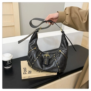 Détail du sac hobo en cuir noir avec rivets dorés, boucle en métal et pompon sur le zip