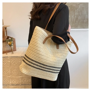 Detail of hand-woven beige straw tote bag with black stripes and brown leather straps