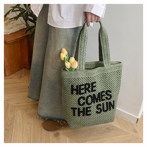 Detail of green woven tote bag with Here Comes The Sun embroidery and hollow mesh texture