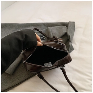 Close-up of the dark brown glossy leather handbag showing black lining and zipper detail