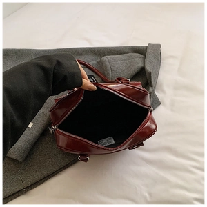 Detail shot of deep red glossy patent leather handbag with silver zipper and spacious interior