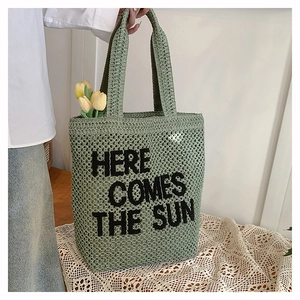 Detail of green woven tote bag featuring black Here Comes The Sun embroidery and tulips