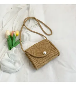 Detail of woven straw crossbody bag featuring a decorative pearl clasp and shoulder strap