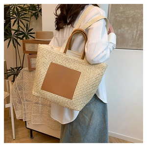 Close-up of woven straw tote bag featuring brown leather handles and square patch detail
