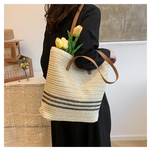 Detail of a beige woven beach tote with black stripes and brown leather handles on a model