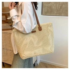 Model showing large beige straw tote bag with brown leather handles in a chic room