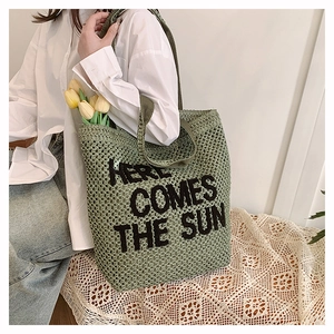 Detail of green woven tote bag with Here Comes The Sun text and long shoulder strap