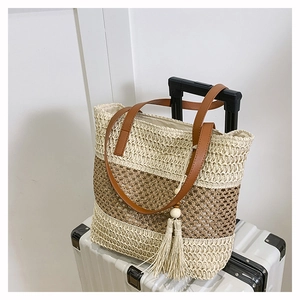 Striped woven straw tote bag with brown leather handles and large tassel on travel case