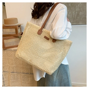 Detail of hand-woven straw tote bag with brown leather shoulder strap shown on model