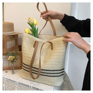 Detail of hand-woven straw tote bag with black stripes and brown leather handles