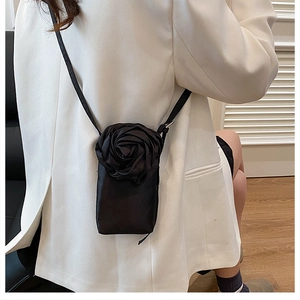 Détail d'un sac bandoulière noir avec rose 3D porté sur un blazer blanc chic